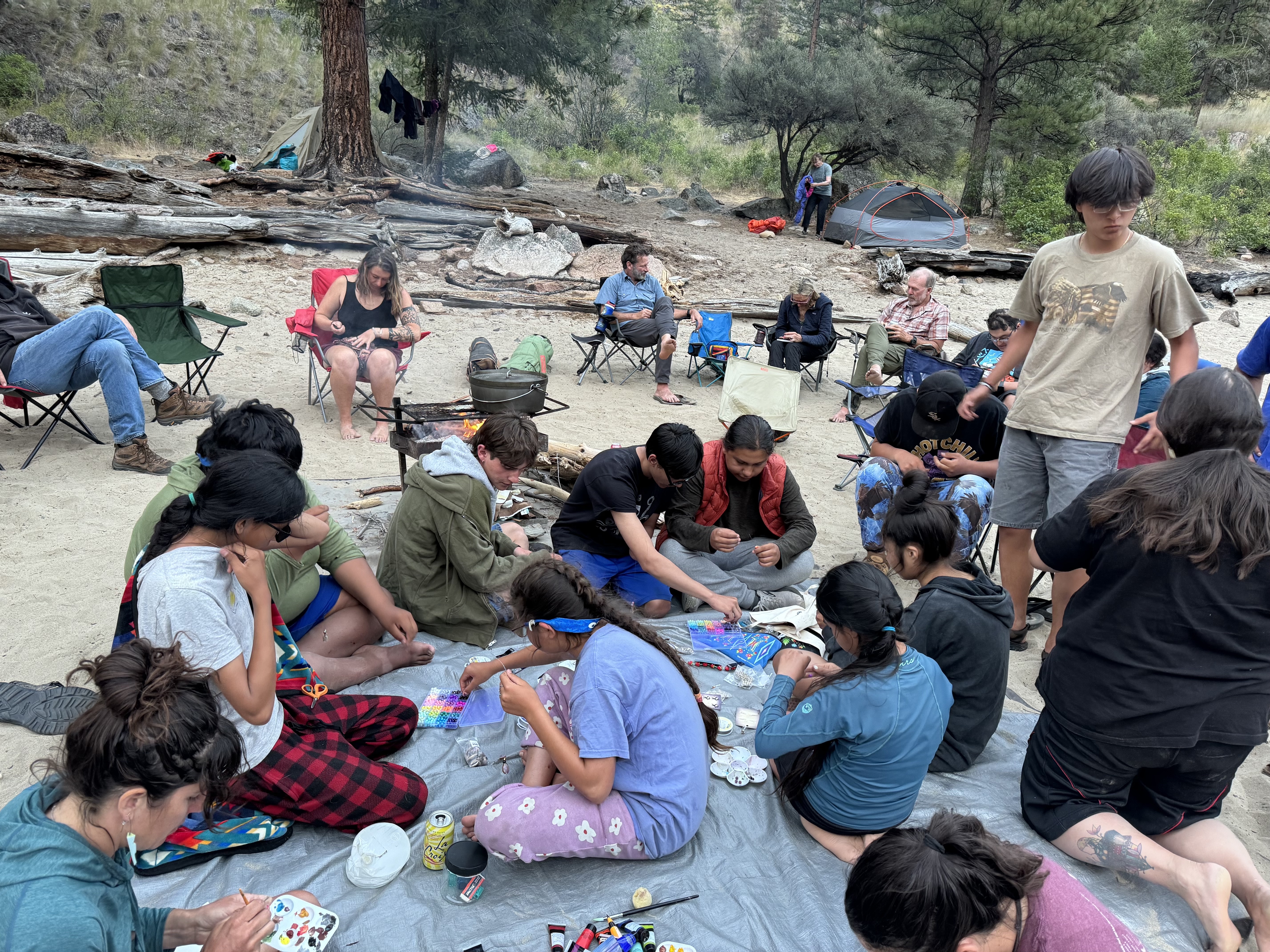 A large group sits on the ground together outside